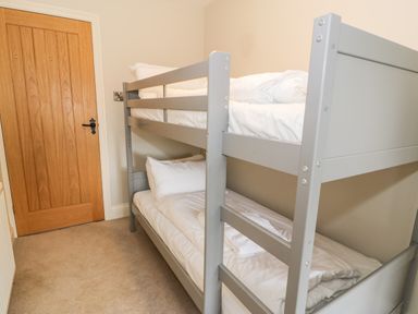 A small bedroom with a grey bunk bed and a wooden door at Lakeside Cottage in Llanrug