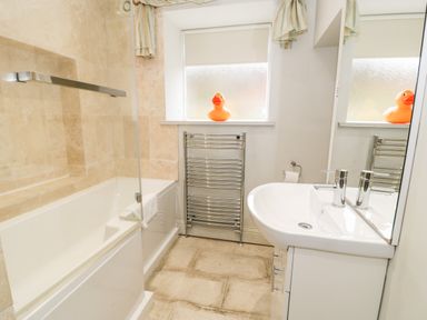 A bathroom with a bathtub shower combination a white sink with a mirror a window with a rubber duck and a towel radiator at Lakeside Cottage in Llanrug