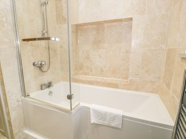 A bathroom with a bathtub shower combination and tiled walls at Lakeside Cottage in Llanrug
