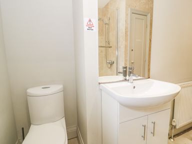 A bathroom with a toilet sink with cabinet and mirror showing a shower area at Lakeside Cottage in Llanrug