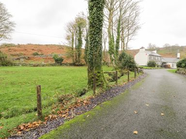 A driveway next to a grassy field with trees and a house in the background at Lakeside Cottage in Llanrug