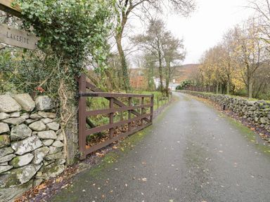 A country road with a wooden gate and stone walls leading to a house at Lakeside Cottage in Llanrug