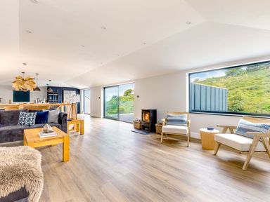 A living room with wooden floor two chairs a small table and a fireplace next to large windows at Breakers View in Polzeath
