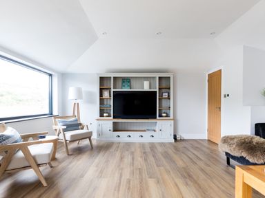 A living room with two wooden armchairs a floor lamp a wooden entertainment unit with a television and a wooden door at Breakers View in Polzeath