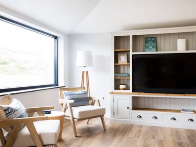 A living room with two wooden armchairs and a large window at Breakers View in Polzeath