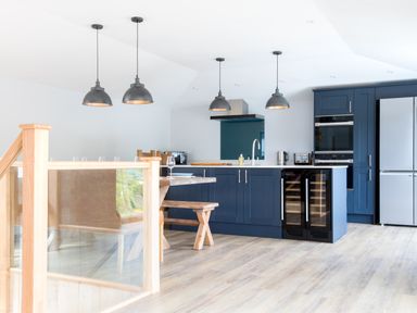 A kitchen with blue cabinets a wooden dining table and hanging lights at Breakers View in Polzeath
