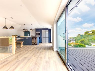 A kitchen with blue cabinets and pendant lights beside a glass door opening to a deck with a view at Breakers View in Polzeath