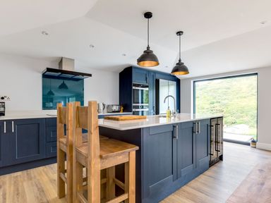A modern kitchen with wooden chairs a large island and a window view at Breakers View in Polzeath