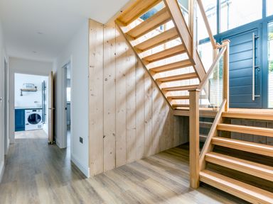 A hallway with wooden stairs and a doorway leading to a laundry room with a washing machine at Breakers View in Polzeath