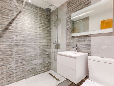 A bathroom with a walk in shower a white vanity with faucet a large mirror and a toilet at Breakers View in Polzeath