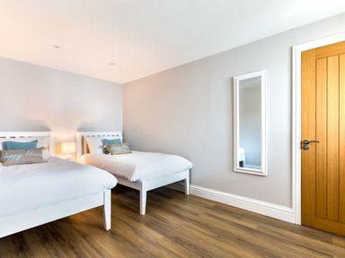 A bedroom with two single beds a wooden floor a wall mirror and a wooden door at Breakers View in Polzeath