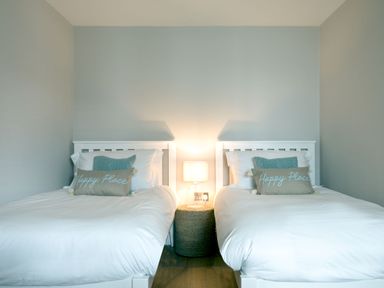 A bedroom with two white beds and a lamp on a round nightstand at Breakers View in Polzeath