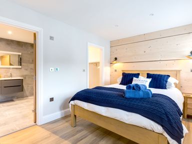 A bedroom with a wooden bed blue pillows and blanket an open door to a bathroom at Breakers View in Polzeath
