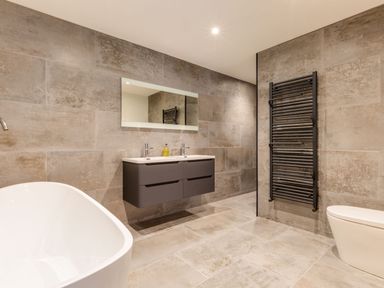 A bathroom with a freestanding bathtub a wall-mounted sink with two faucets a large mirror a towel radiator and a toilet at Breakers View in Polzeath