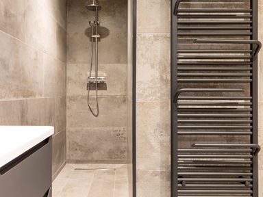 A shower area with large tiles a shower head and a black heated towel rail in the bathroom at Breakers View in Polzeath