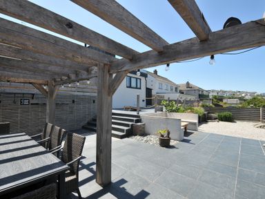 A garden with a wooden pergola and dining table at Breakers View in Polzeath