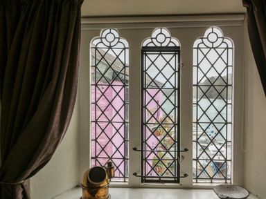 A window with lattice design overlooking pink buildings and a harbor at 1 The Old Brewhouse in Dartmouth