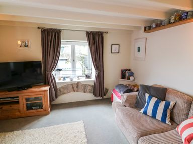A living room with a sofa with striped cushions a television on a wooden cabinet and curtains on a window at 1 The Old Brewhouse in Dartmouth