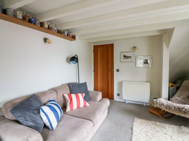 A living room with a beige sofa with cushions and a wooden door at 1 The Old Brewhouse in Dartmouth