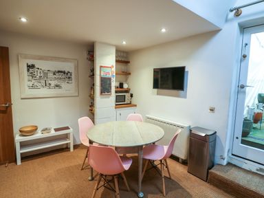 A dining area with a round table and four pink chairs near a wall-mounted TV and a door at 1 The Old Brewhouse in Dartmouth