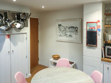 A kitchen with hanging pots and pans a round table with pink chairs a wooden bowl and wall art at 1 The Old Brewhouse in Dartmouth