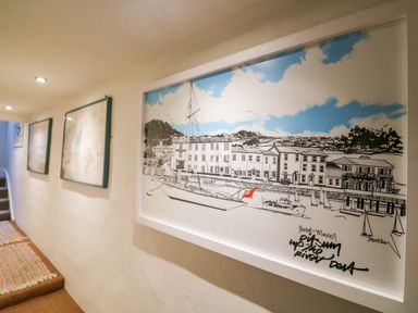 A hallway with framed artwork and maps on the wall and a carpet runner on the floor at 1 The Old Brewhouse in Dartmouth