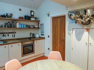 A kitchen with wooden countertops hanging pots a round table and shelves with kitchen utensils at 1 The Old Brewhouse in Dartmouth