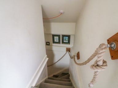 A stairway with a rope handrail on the wall and framed pictures at the bottom at 1 The Old Brewhouse in Dartmouth