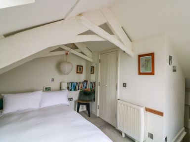 A bedroom with a white bed pillows a hanging paper lantern books on a shelf a chair and framed pictures at 1 The Old Brewhouse in Dartmouth