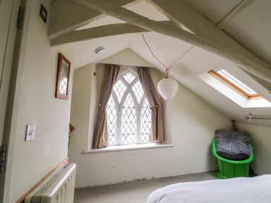A bedroom corner with a green chair with a cushion and a window with curtains at 1 The Old Brewhouse in Dartmouth