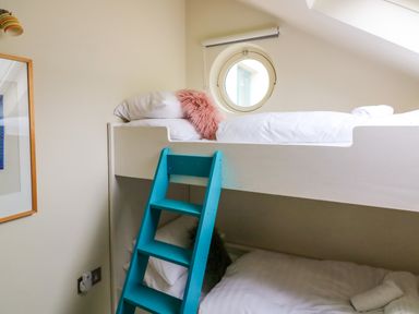 A bunk bed with a blue ladder and round window in a bedroom at 1 The Old Brewhouse in Dartmouth