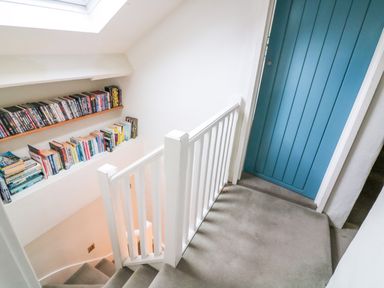 A staircase with white railing and built in shelves holding books and dvds next to a blue door at 1 The Old Brewhouse in Dartmouth