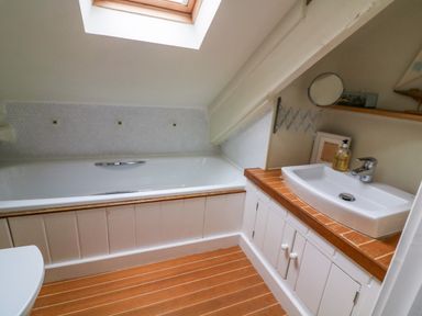A bathroom with a bathtub under a skylight and a sink on a wooden countertop with cabinets below at 1 The Old Brewhouse in Dartmouth