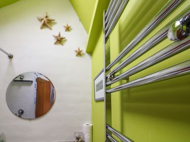 A bathroom with a round mirror starfish wall decorations and a chrome towel radiator at 1 The Old Brewhouse in Dartmouth