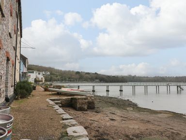 A waterfront path next to stone buildings with boats and a pier over water at 1 The Old Brewhouse in Dartmouth