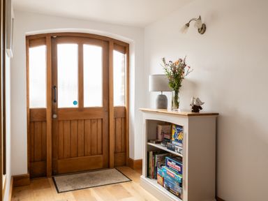 A hallway with a wooden door and a shelf displaying board games at Hoppers Barn Pancrasweek near Holsworthy