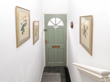 A hallway with a green door at the end with framed botanical prints on white walls and a striped rug on the floor at 60B Castlegate in Berwick-Upon-Tweed