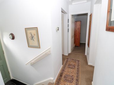 A hallway with a patterned runner rug a wall clock floral picture and a wooden wardrobe visible through an open door at 60B Castlegate in Berwick-Upon-Tweed