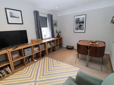 A living room with a television on wooden shelves and a dining table with chairs at 60B Castlegate in Berwick-Upon-Tweed