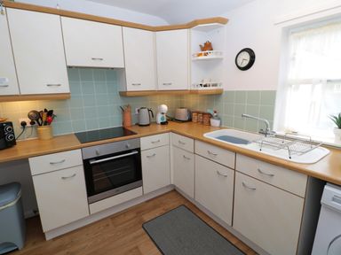 A kitchen with wooden countertops white cabinets a built in oven a sink under a window and kitchen appliances at 60B Castlegate in Berwick-Upon-Tweed