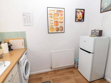 A kitchen corner with a washing machine under a countertop and a white fridge with a radio on top at 60B Castlegate in Berwick-Upon-Tweed