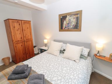 A bedroom with a bed with patterned bedding and pillows two bedside tables with lamps a wooden wardrobe and a framed picture on the wall at 60B Castlegate in Berwick-Upon-Tweed
