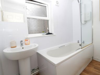 A bathroom with a white bathtub a shower a pedestal sink and a frosted window at 60B Castlegate in Berwick-Upon-Tweed