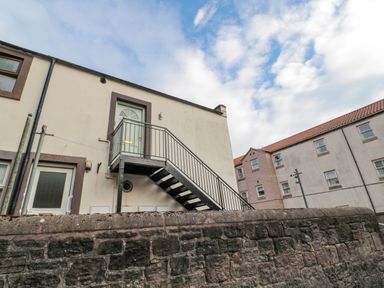 An exterior view of a building with a metal staircase leading to a door on the first floor and a stone wall in front at 60B Castlegate in Berwick-Upon-Tweed