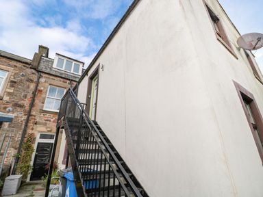 An exterior staircase leading to an upper door of a white building next to a stone building with windows at 60B Castlegate in Berwick-Upon-Tweed