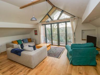 A living room with sofas a coffee table a rug and a television near large windows with curtains at Green Grove Barn in Peniel near Carmarthen