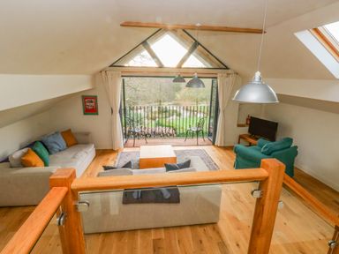 A living room with sofas a coffee table and a balcony overlooking a garden at Green Grove Barn in Peniel near Carmarthen