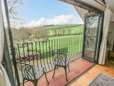 A balcony with two black chairs and metal railing overlooking green fields and trees at Green Grove Barn in Peniel near Carmarthen