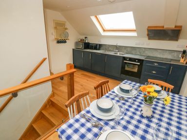 A kitchen with blue cabinets a dining table set with bowls plates glasses and flowers at Green Grove Barn in Peniel near Carmarthen