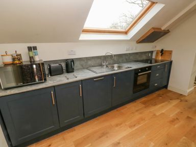 A kitchen with dark cabinets a built in oven sink microwave kettle and toaster under a skylight window at Green Grove Barn in Peniel near Carmarthen